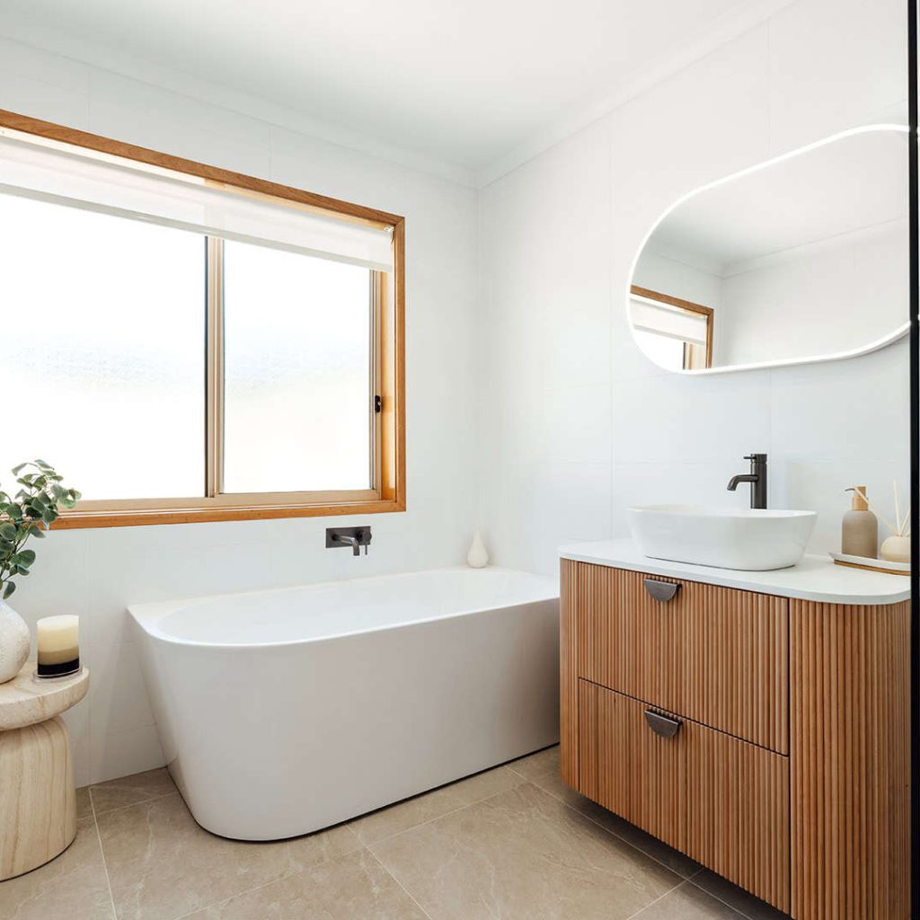Bright and airy bathroom featuring a sleek white bathtub, wooden vanity, and large window for natura.
